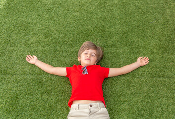 Relaxed boy in red t-shirt lying on artificial grass