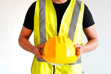 Young slim young contractor with safety vest and safety helmet in hand, on white background, model not recognized.