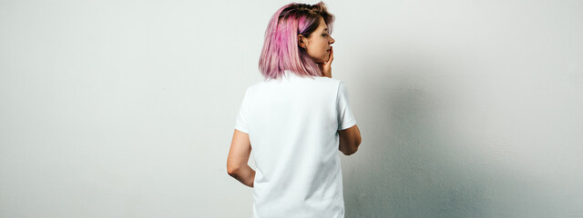 Pretty plus size model with white blank t-shirt and pink hear, empty grunge wall background. Back view