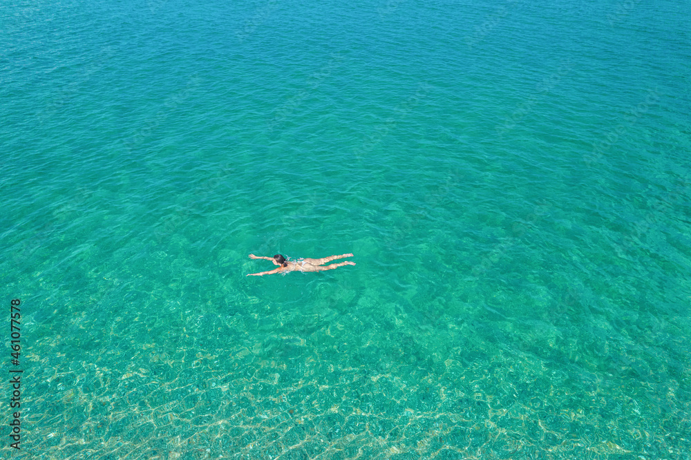 Young woman in a bikini swimming in sea water on the beach. View from ...