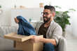 © Prostock-studio - Satisfied Arab male client taking out new clothes from cardboard box, happy with delivery service at home