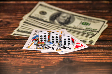 Dice, dollars and playing cards on a dark wooden background, money gambling.