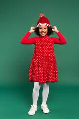 Full length of smiling african american girl in red dress wearing hat on green background