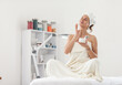 © splitov27 - Beautiful cute Caucasian woman wrapped in a towel sits on a couch and applies cream to her face in beauty salon. Skin care