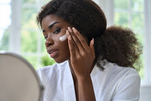 Attractive Young Black African Woman Model Touching Healthy Flawless Radiant Smooth Face Skin Care Looking In Bathroom Mirror Applying Facial Cream. Ethnic Beauty Skincare Morning Routine Concept