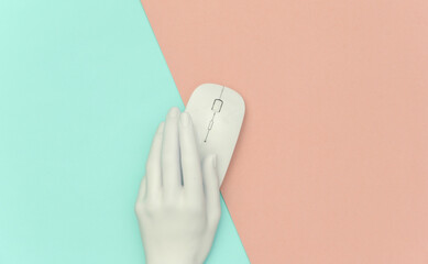 Wall Mural - The mannequin's white hand holding pc mouse on pink blue pastel background. Top view