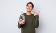 young hispanic man smiling confidently pointing to own broad smile. water bottle concept