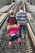 Humorous funny photo of sister girl child left behind by her oblivious brothers in mid air tripping falling on train tracks without them knowing she fell ignoring her.