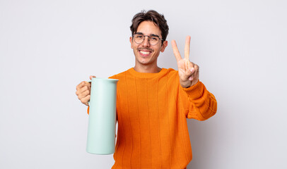 young hispanic man smiling and looking friendly, showing number two. thermos concept