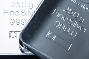 Two silver bars weighing 250 grams each, under different lighting. Selective focus.