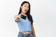 Happy modern asian girl showing credit card and winking at camera, recommending bank, standing over white background
