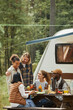 © Seventyfour - Vertical shot of diverse group of friends enjoying picnic outdoors at campsite with trailer van