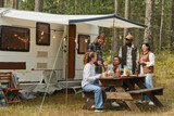Fototapeta  - Wide angle view at diverse group of young people enjoying picnic outdoors while camping with trailer van, copy space