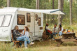 Wide angle view at group of young people relaxing outdoors by camper van in autumn, copy space