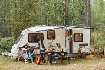 wide angle view of young people enjoying outdoors while camping with van in forest, copy space