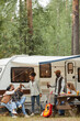 © Seventyfour - Vertical full length portrait of friends enjoying outdoors while camping with van in forest, copy space