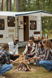 Fototapeta  - Vertical full length portrait of young people roasting marshmallows while enjoying camping with friends in forest