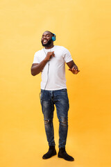 Wall Mural - Full length portrait of a cherry young african american man listening to music with headphones and dancing isolated over yellow background