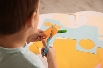 Sticker - Little boy cutting color paper with scissors at table indoors, closeup