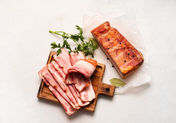 Wooden board with slices of tasty smoked bacon on light background