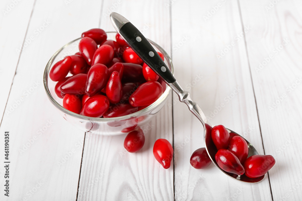 Bowl with fresh dogwood berries on light wooden background