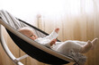 © KDdesignphoto - Cute smiling baby laying in bouncer chair. Child relaxing in a swing. Adorable newborn baby in bodysuit in sunny bedroom. Family morning at home.
