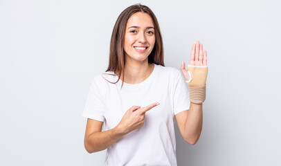 Poster - young pretty woman smiling cheerfully, feeling happy and pointing to the side. hand bandage concept