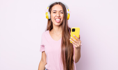 Poster - young pretty woman with cheerful and rebellious attitude, joking and sticking tongue out. headphones and smartphone