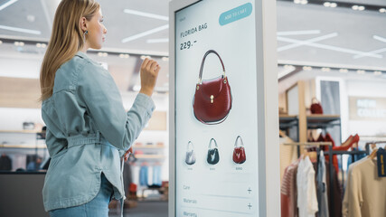 Poster - Beautiful Female Customer Using Floor-Standing LCD Touch Display while Shopping in Clothing Store. She is Choosing Stylish Bags, Picking Different Designs from Collection. People in Fashionable Shop.