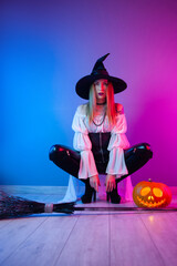 a girl in a witch costume for Halloween with a broom and a pumpkin in neon light