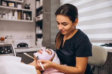 cosmetologist applying mask on a face of client in a beauty salon