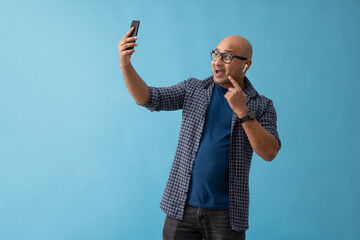 Wall Mural - Portrait of a bald man with bluetooth in his ears video calling on mobile phone.