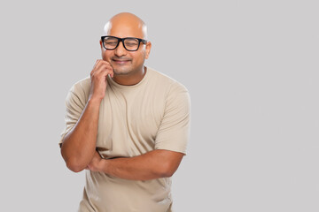 Wall Mural - Portrait of a bald man wearing eyeglasses smiling while thinking something with closed eyes against plain background.