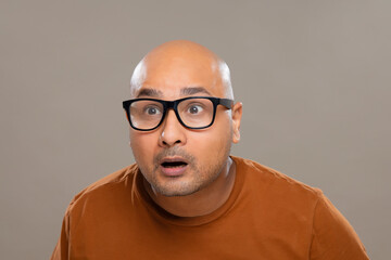Wall Mural - Portrait of a bald man wearing eyeglasses gaping with amazed expression against plain background.