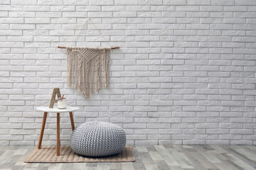 Sticker - Comfortable knitted pouf, table and decor elements near white brick wall indoors, space for text. Interior design