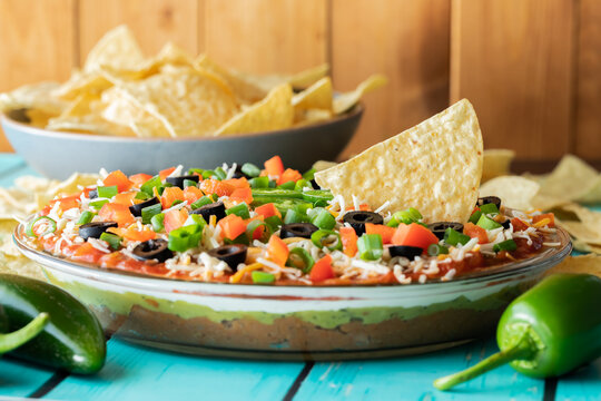Close up of a Mexican layered dip with a bowl of nacho chips in behind. 