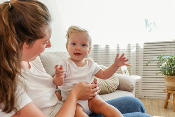 Wall Mural - Portrait of a loving young mother holding her toddler child. Woman with her blonde child having fun at home. Close up, copy space for text, background.