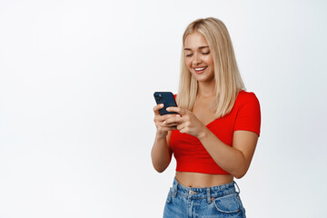 Wall Mural - Cellular technology. Young blond woman using mobile phone and smiling, messaging or placing an oder on smartphone, white background