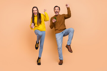 Poster - Full length photo of brunette astonished couple hold telephones wear sweaters jeans shoes isolated on beige background