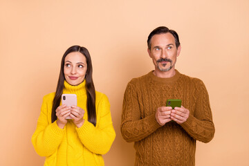 Wall Mural - Photo of brunette interested couple hold telephones look empty space wear knit sweaters isolated on beige background