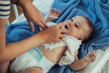 an anonymous mother having fun while dressing up her little baby boy in a bed. unrecognizable mother