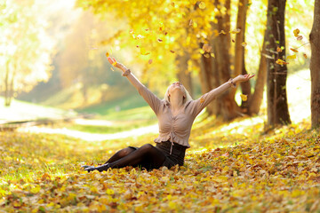 blonde girl in street clothes sitting in a heap of autumn leaves