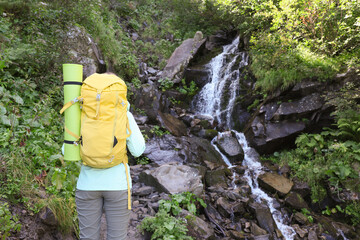 Canvas Print - Tourist with backpack near stream in mountains, back view. Space for text