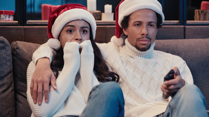 Wall Mural - African american man watching movie with scared girlfriend in santa hat