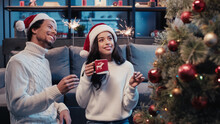 Joyful African American Couple In Santa Hats Holding Cup And Sparklers While Looking At Blurred Christmas Tree