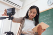 Asian Young Female teacher using digital tablet and digital camera for online teaching.