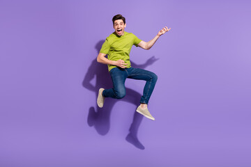 Poster - Full size photo of cool young brunet guy jump play guitar wear t-shirt jeans sneakers isolated on violet background