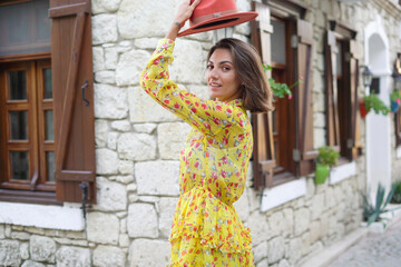 Wall Mural - A beautiful young woman with a hat in a dress on a cute cozy Turkish street is having fun walking, spinning, posing, smiling