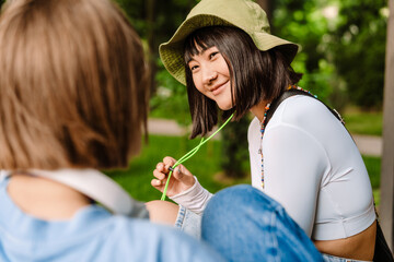 Multiracial two women talking and smiling while resting in park