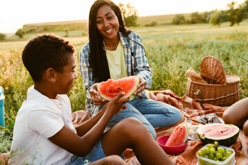 Wall Mural - Black family eating watermelon during picnic on summer field